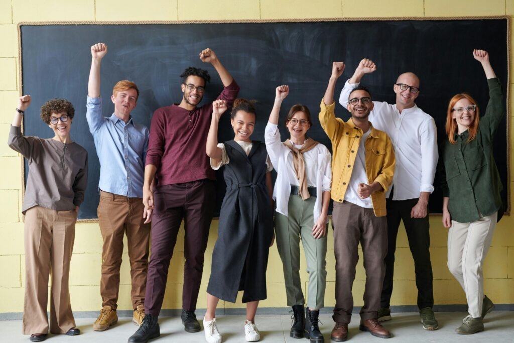 A group of eight adults cheerfully standing with raised fists in front of a blackboard indoors.